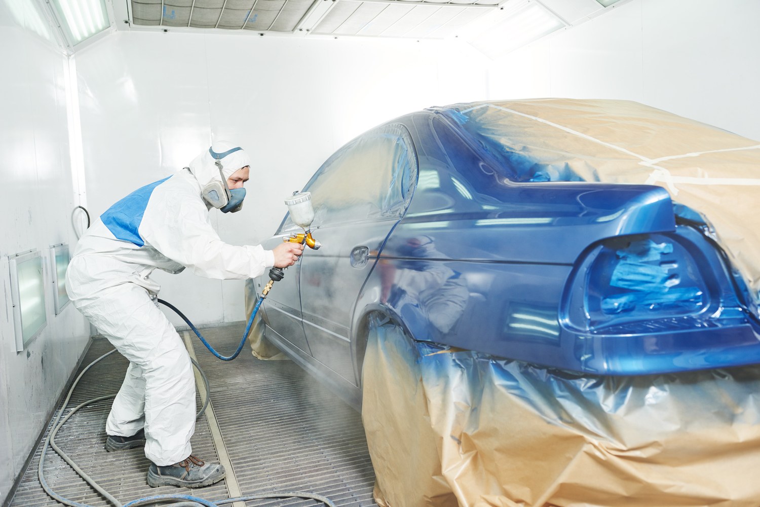 Verniciatore in tuta protettiva al lavoro sulla carrozzeria di un'automobile in cabina